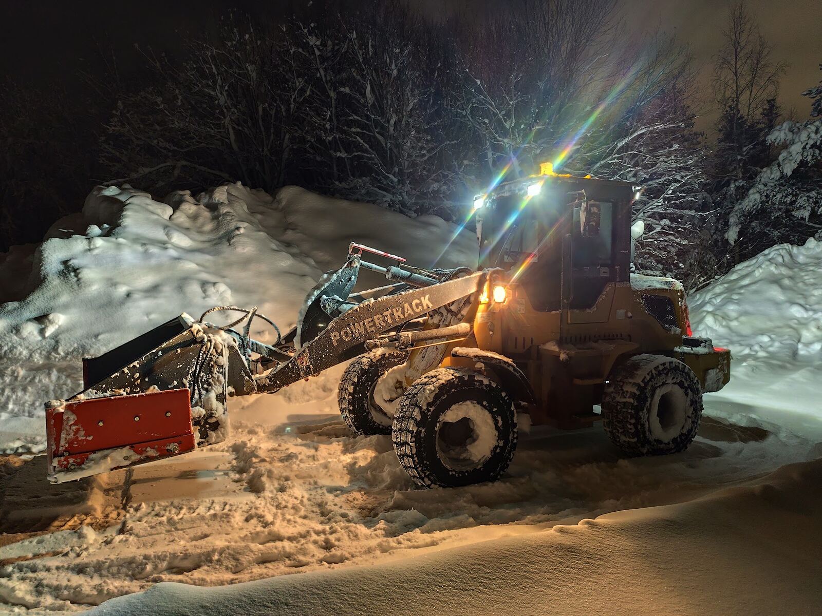 Hjullaster med plog og skuffe brøyter snø om natta